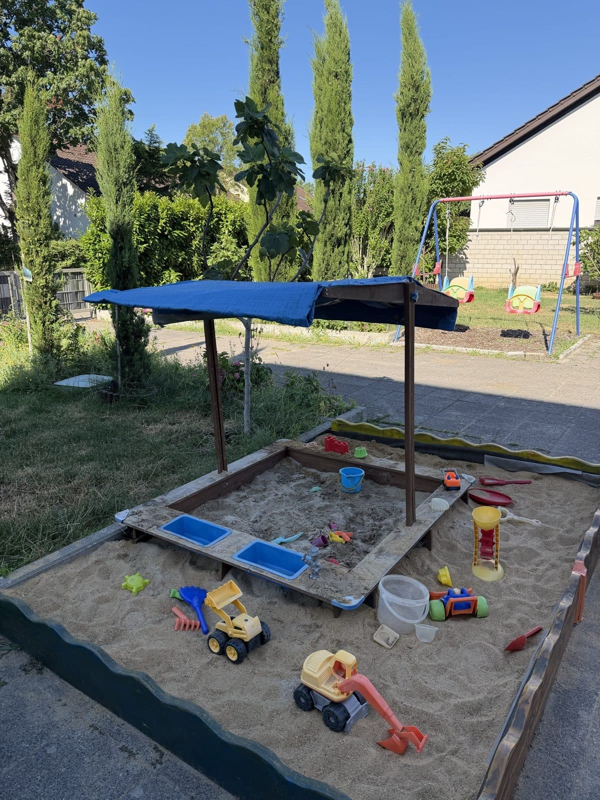 Der Garten mit Schaukel, überdachtem Sandkasten und viel Grün